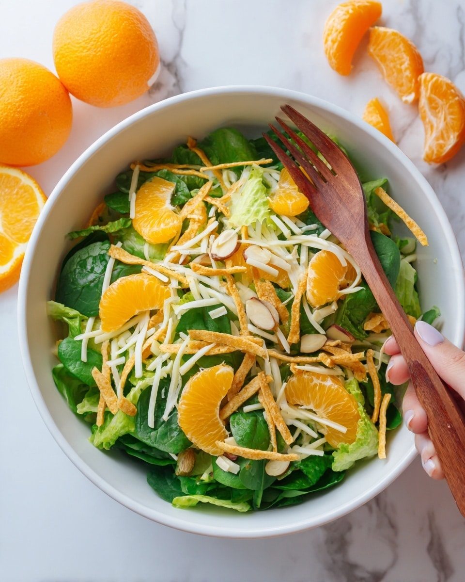 A white bowl filled with a fresh salad featuring multiple layers starting with a base of green leafy lettuce and spinach that cover the bowl evenly, topped with bright orange slices of mandarin arranged throughout. On top of the greens and oranges are shredded white cheese and thin crispy golden-brown fried strips scattered evenly. The salad is sprinkled with small, light yellow almond slices adding texture. The bowl sits on a white marbled surface next to partially visible whole and sliced oranges. A woman's hand holds a wooden fork above the salad. Photo taken with an iphone --ar 4:5 --v 7