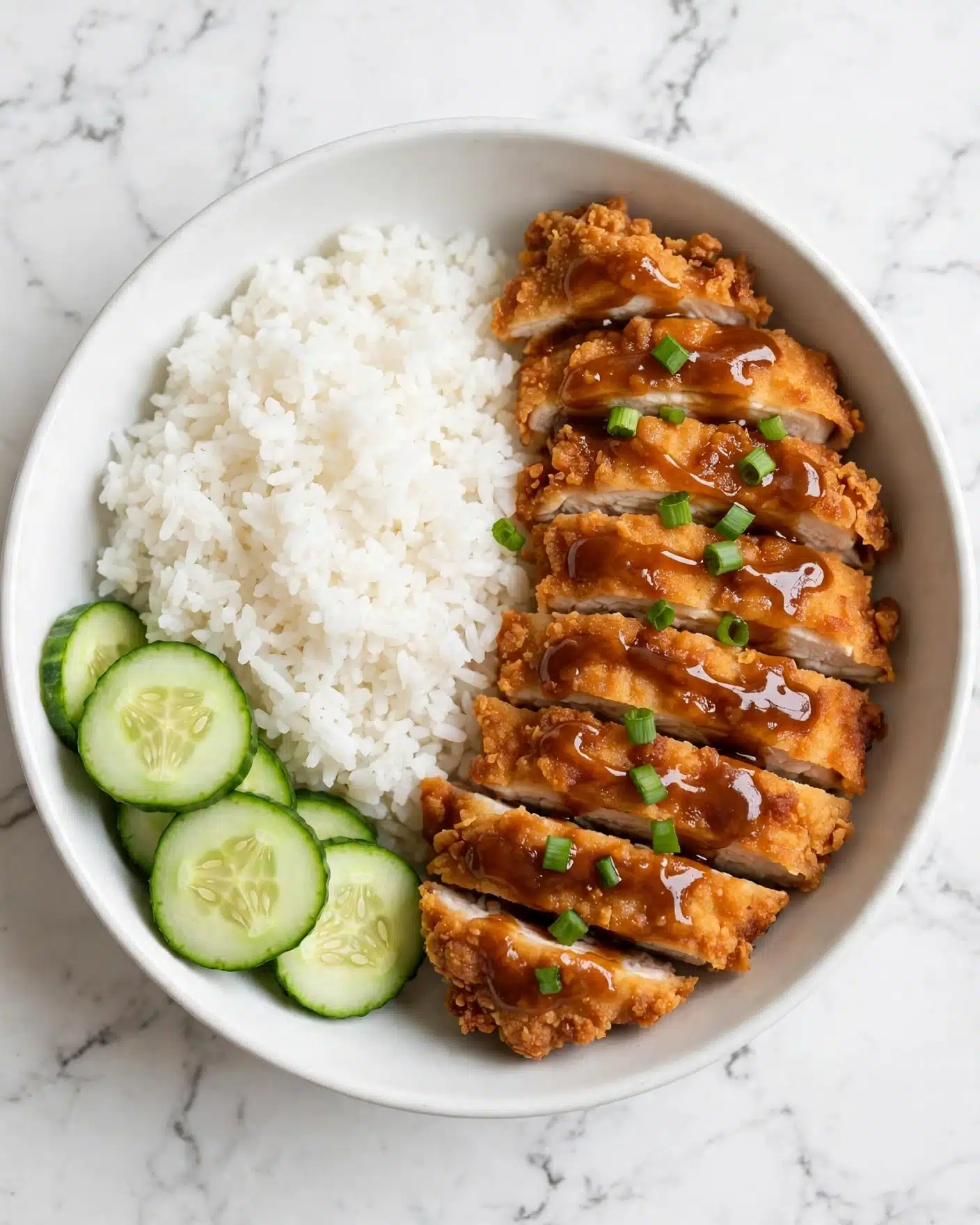 square image A white bowl with steamed white rice on the left side and crispy golden-brown fried chicken slices placed on the right side, arranged neatly in a row. The chicken has a crunchy texture with a shiny brown sauce drizzled on top, sprinkled with small green chopped onions. In the background, fresh green cucumber slices are placed next to the rice, adding a fresh look. The background is a white marbled texture. Photo taken with an iphone --ar 4:5 --v 7
